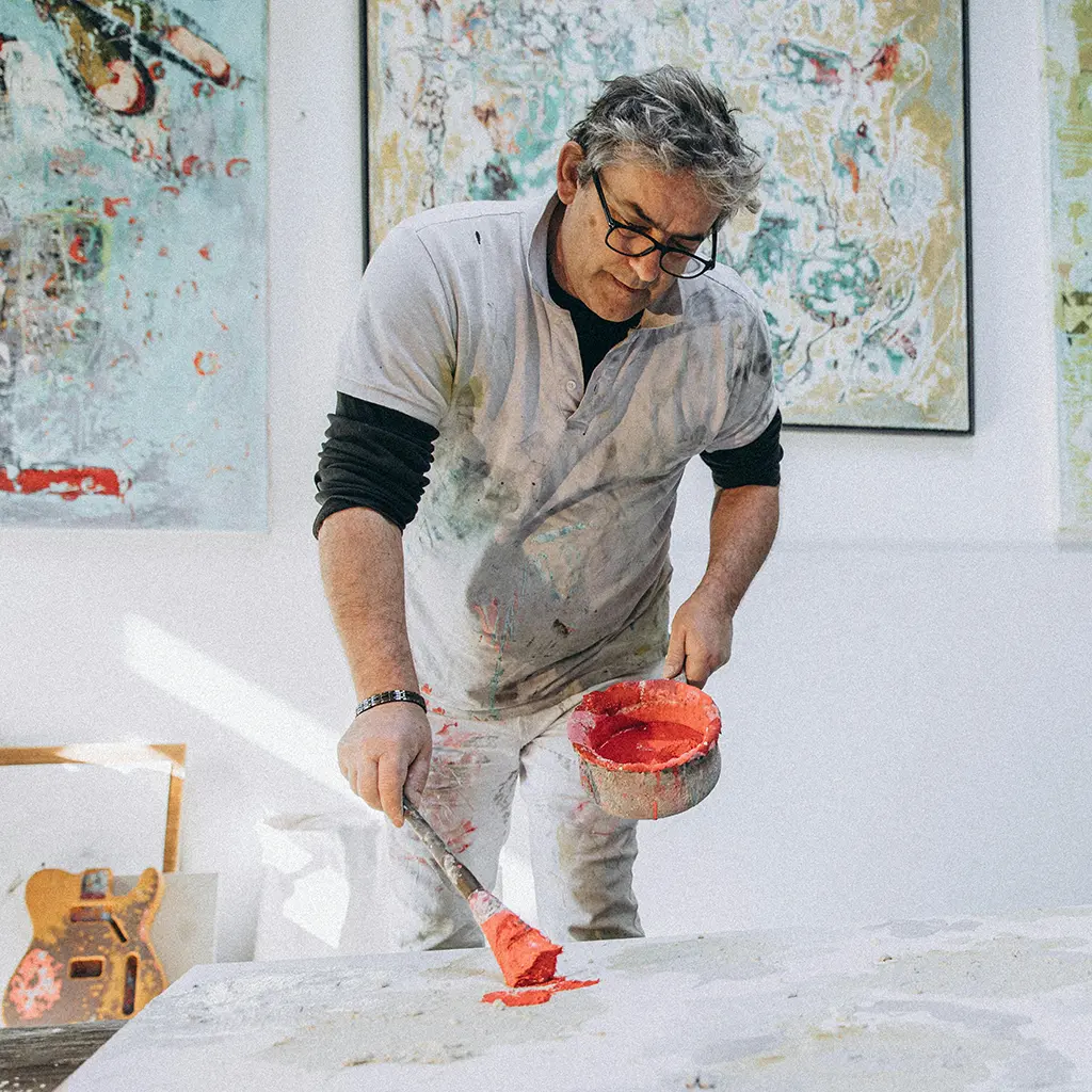 Artist applying red paint to a canvas in a studio, surrounded by abstract artworks